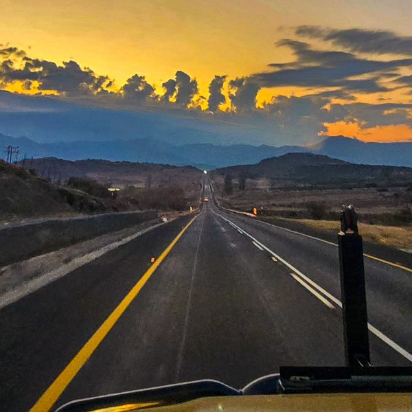 Open two-lane highway at dawn seen over a truck hood, orange cloud on the horizon