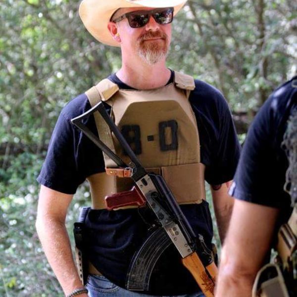 Jon Wayne Taylor in a cowboy hat and plate carrier with a slung AK-pattern rifle